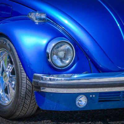 A close-up of the front end of a classic Volkswagen beetle, metallic blue.